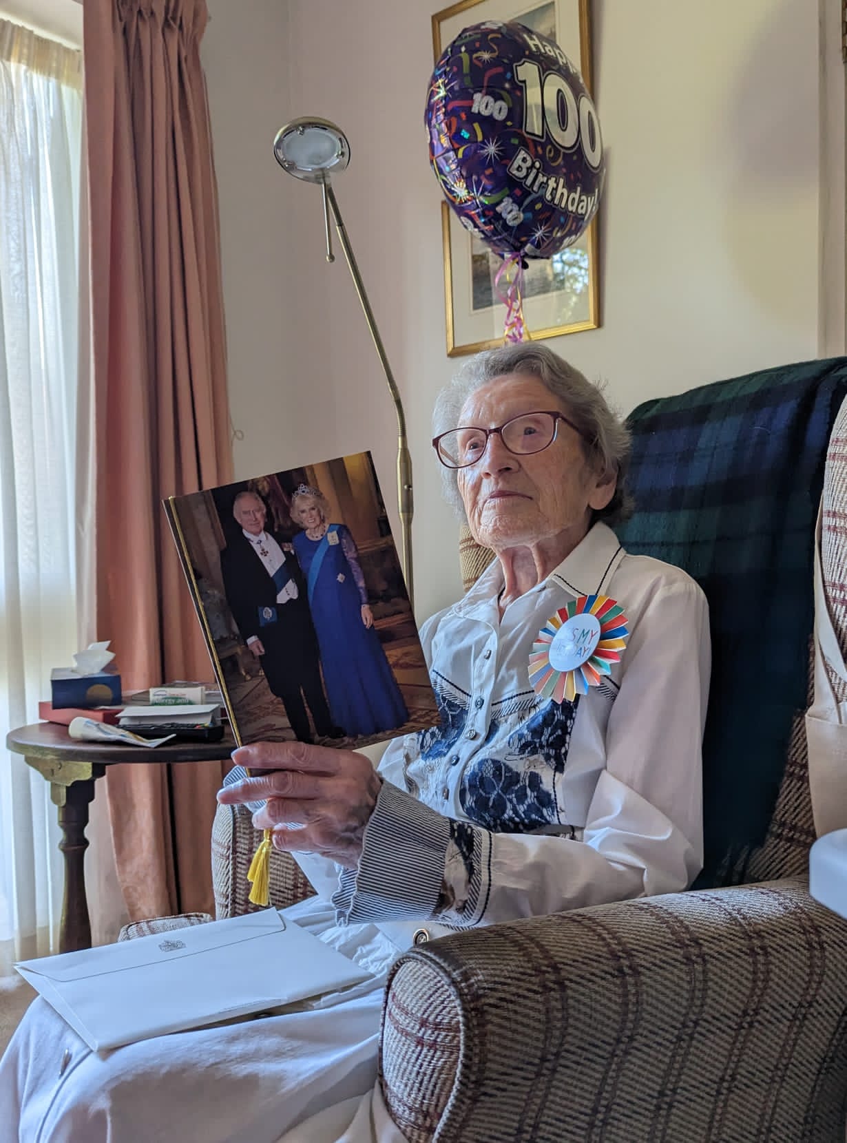 Lady celebrating her 100th birthday, holding her card from HRH King Charles